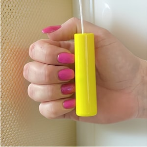 May include: A bright yellow plastic pull cord for blinds or curtains. The cord is held in a hand with pink nail polish.