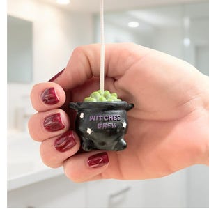 May include: A black cauldron-shaped light pull with the words "Witches Brew" and star accents. The cauldron is filled with green, bubbling liquid. A white cord extends from the top.
