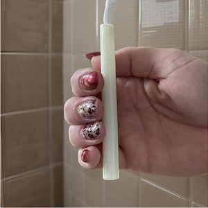 Könnte beinhalten: Ein weißer, zylindrischer Menstruationsbecher mit einer weißen Schnur, die an der Oberseite befestigt ist. Der Becher wird in einer Hand mit rotem und leopardenfarbenem Nagellack gehalten.