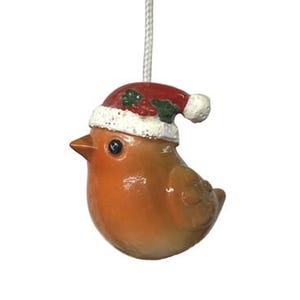Könnte beinhalten: Ein keramischer Rotkehlchen-Ornament mit rotem Weihnachtsmannhut mit weißem Rand und grünem Stechpalmenblatt. Der Vogel hat einen glänzenden orangefarbenen Körper und einen kleinen Schnabel. Eine weiße Schnur ist zum Aufhängen befestigt.