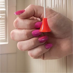 May include: A hand with pink nail polish is pulling a bright orange cord with a round, orange pull.