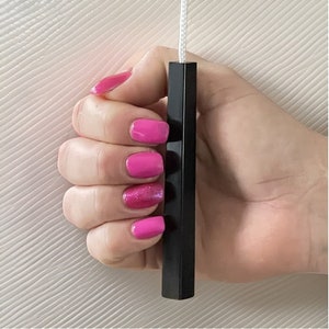 Può includere: Un tiretto quadrato nero per un apparecchio di illuminazione. Il tiretto è tenuto da una mano con smalto rosa.