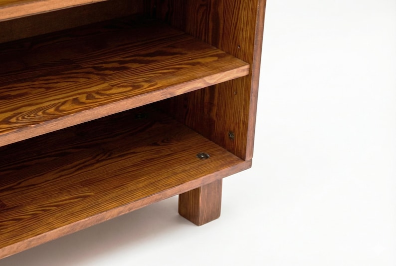 May include: A wooden bookshelf with two visible shelves. The shelves and sides are made of a warm-toned wood, showcasing a prominent wood grain pattern. The bookshelf has a simple, sturdy design, with a rectangular base.