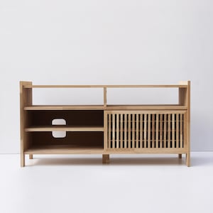 May include: A light-coloured wooden media console with open shelving and a cabinet with vertical slat detailing. The console has a rectangular shape and is designed for a modern living room. It features multiple shelves and a cabinet for storage.