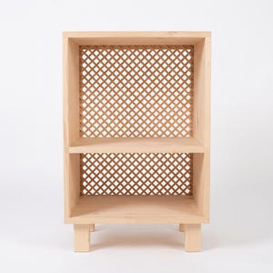 May include: A light-colored wooden shelf unit featuring two open storage levels. The back panel of each section is constructed with a decorative lattice pattern made of thin wooden strips arranged in a diamond grid, supported by four short legs.