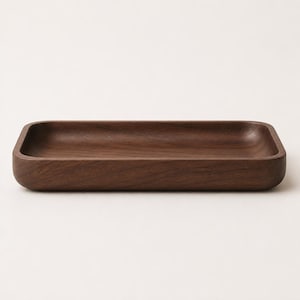 May include: A rectangular wooden tray with rounded corners and a smooth, dark brown finish. The tray features a shallow, recessed center and thick, solid walls, showcasing the natural grain patterns of the wood throughout the entire surface.