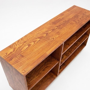 May include: A rectangular wooden bookshelf with a warm, reddish-brown finish. The bookshelf has multiple shelves and a natural wood grain pattern. The design is simple and modern, suitable for various home decor styles.
