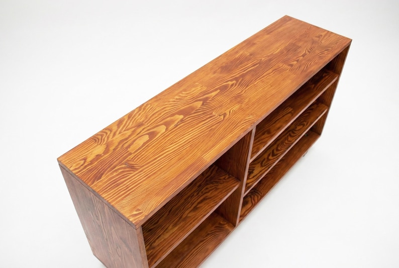 May include: A rectangular wooden bookshelf with a warm, reddish-brown finish. The bookshelf has multiple shelves and a natural wood grain pattern. The design is simple and modern, suitable for various home decor styles.