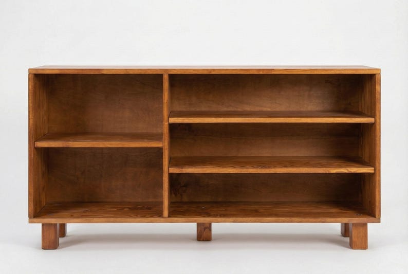 May include: A wooden bookcase with a warm brown finish. The bookcase has two sections, one with two shelves and the other with three shelves. The unit is supported by short, rectangular legs. Ideal for storage.