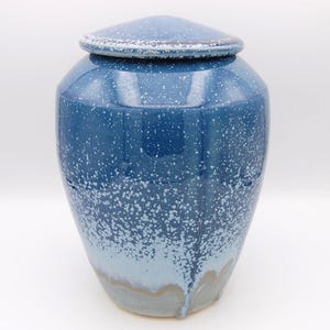 May include: A ceramic urn with a lid, featuring a glossy finish that transitions from a deep navy blue at the top to a lighter sky blue at the base. The surface is covered in a white speckled pattern that resembles a starry night sky.