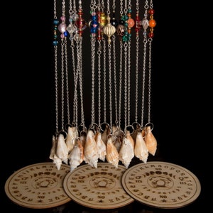 May include: A set of 18 silver chains with seashells hanging from them. The chains are decorated with colourful beads. The seashells are hanging over three wooden Ouija boards.