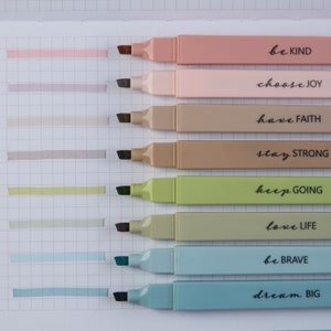 May include: Set of eight highlighters with motivational phrases. The highlighters are in shades of pink, beige, green, and blue. The phrases are "be KIND", "choose JOY", "have FAITH", "stay STRONG", "keep GOING", "love LIFE", "be BRAVE", and "dream BIG".