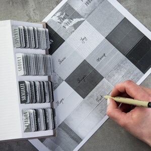 May include: A black and white grid with different words written in black ink. The words are: Genesis, Exodus, Leviticus, Numbers, 1 John, 3 John, Peace, Joy, Mercy, Hope, Prayer, Faith. A hand is holding a pen and writing the word "Faith" in one of the squares.