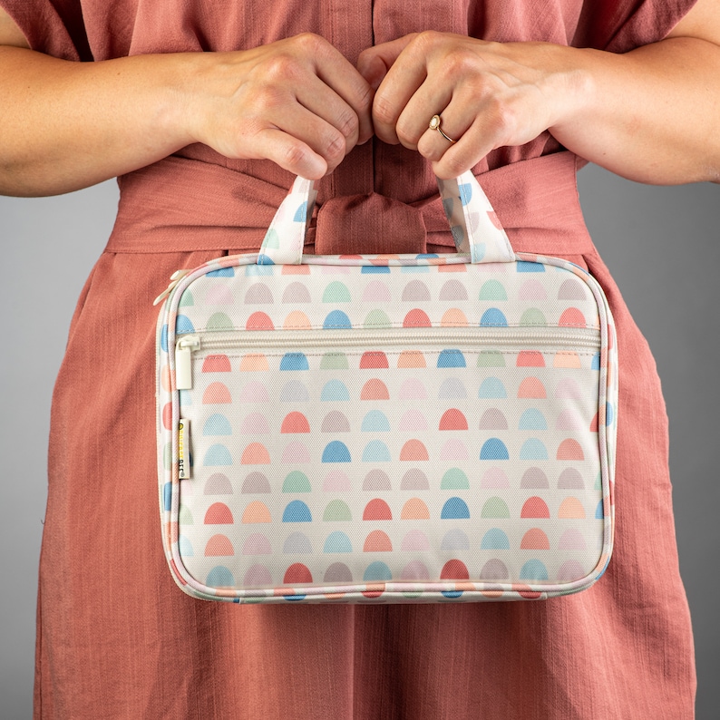 May include: A white toiletry bag with a colorful half-circle pattern. The bag has a zipper closure and a top handle.