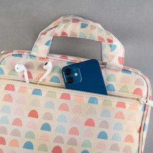 May include: A white and pink patterned zippered pouch with a blue phone and white earbuds inside.