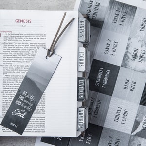 May include: A close-up of a black and white bookmark with a forest scene and the text "Act justly, love mercy, walk humbly with God". The bookmark is placed in a Bible with tabs for each book of the Bible.