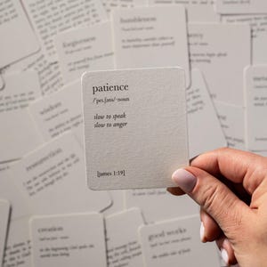 May include: A square off-white card with a textured surface featuring the word patience, its phonetic spelling, the definition slow to speak slow to anger, and the citation James 1:19 printed in black text, surrounded by other similar cards.