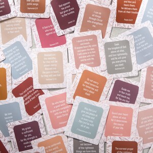 Pu&ograve; includere: Una collezione di carte quadrate colorate con angoli arrotondati, ognuna con un versetto biblico in testo bianco. Le carte hanno un design floreale sullo sfondo. La tavolozza dei colori comprende sfumature di rosa, arancione e blu.