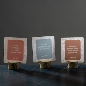Pu&ograve; includere: Tre portacarte decorativi in legno con citazioni ispiratrici. Ogni carta ha uno sfondo di colore diverso e un design floreale. Il testo sulle carte include versetti biblici dai Salmi e dagli Efesini.