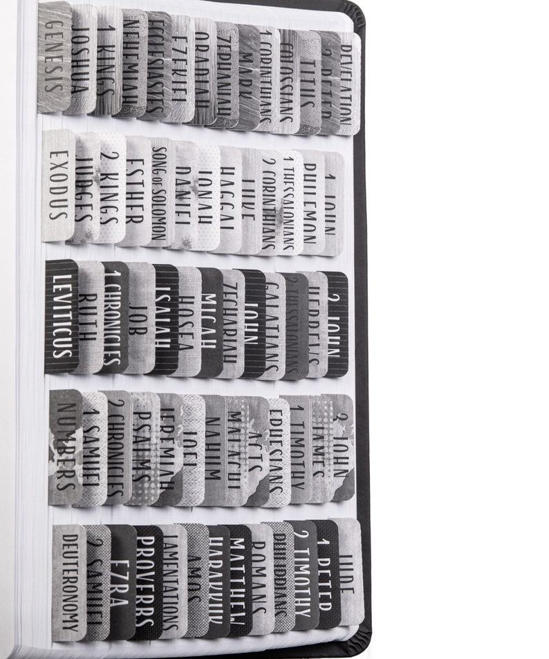 May include: A close-up of a black and white Bible with tabs for each book of the Bible. The tabs are labeled with the names of the books of the Bible, such as Genesis, Exodus, Leviticus, Numbers, Deuteronomy, Joshua, Judges, Ruth, 1 Samuel, 2 Samuel, 1 Kings, 2 Kings, 1 Chronicles, 2 Chronicles, Ezra, Nehemiah, Esther, Job, Psalms, Proverbs, Ecclesiastes, Song of Solomon, Isaiah, Jeremiah, Lamentations, Ezekiel, Daniel, Hosea, Joel, Amos, Obadiah, Jonah, Micah, Nahum, Habakkuk, Zephaniah, Haggai, Zechariah, Malachi, Matthew, Mark, Luke, John, Acts, Romans, 1 Corinthians, 2 Corinthians, Galatians, Ephesians, Philippians, Colossians, 1 Thessalonians, 2 Thessalonians, 1 Timothy, 2 Timothy, Titus, Philemon, Hebrews, James, 1 Peter, 2 Peter, 1 John, 2 John, 3 John, Jude, Revelation.