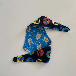 May include: A reversible blue and black bandana with a Star Wars theme. One side features a blue background with white R2-D2 robots and yellow stars. The other side features a black background with yellow circles and a black and white Darth Vader graphic.
