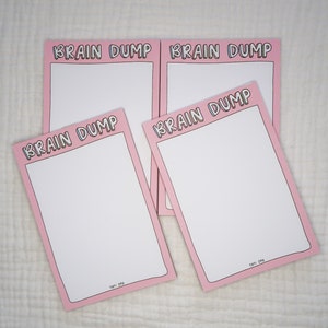 May include: Four pink and white Brain Dump notepads. Each notepad has a pink border and the words "BRAIN DUMP" in a bubble font at the top. The notepads are rectangular with a blank white space for writing.