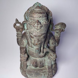 May include: A green bronze statue of the Hindu deity Ganesha, seated with his trunk raised and holding a small object in his hand. The statue is intricately detailed with carvings and has a traditional headdress.