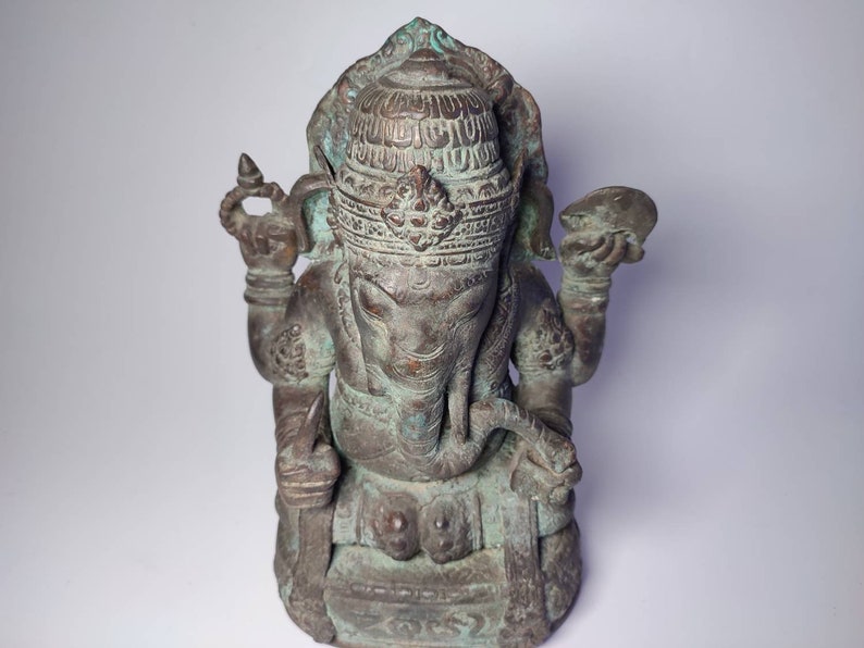 May include: A green bronze statue of the Hindu deity Ganesha, seated with his trunk raised and holding a small object in his hand. The statue is intricately detailed with carvings and has a traditional headdress.