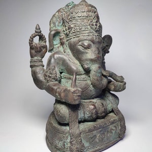 May include: A bronze statue of Ganesha, the Hindu god of wisdom and prosperity, seated on a base with intricate carvings. The statue is detailed with a crown, elephant head, and multiple arms.