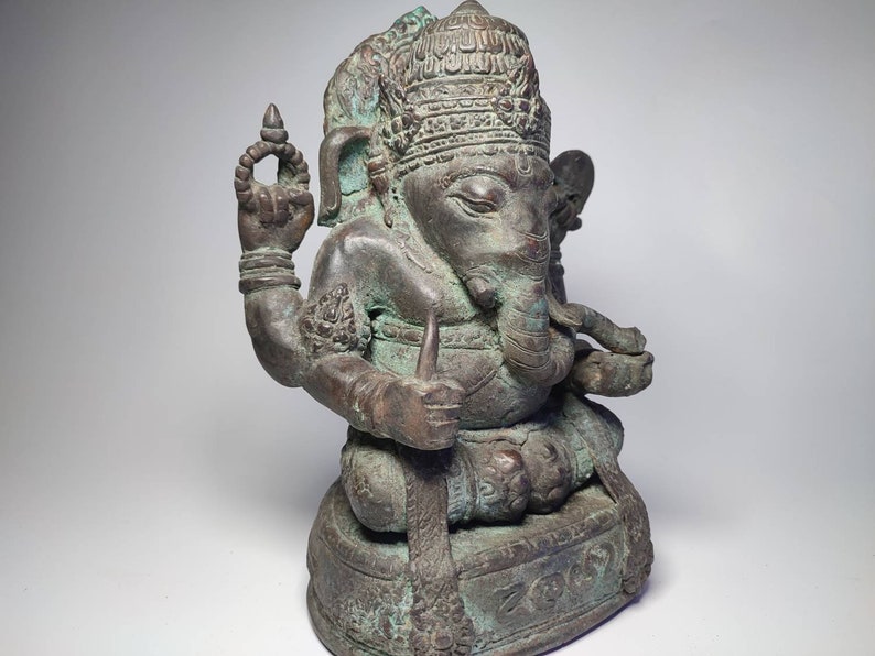 May include: A bronze statue of Ganesha, the Hindu god of wisdom and prosperity, seated on a base with intricate carvings. The statue is detailed with a crown, elephant head, and multiple arms.