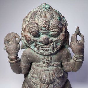 May include: A green and brown bronze statue of a mythical creature with a fierce expression. The statue has intricate details and is holding a round object in one hand and a small object in the other.