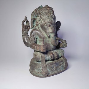 May include: A green bronze statue of Ganesha, the Hindu god of wisdom and prosperity, seated on a base with intricate carvings. The statue has a detailed headpiece and four arms, holding various objects.