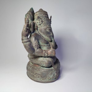 May include: A bronze statue of Ganesha, the Hindu god of wisdom and prosperity, with a detailed headpiece and four arms. The statue is sitting on a base with intricate carvings.