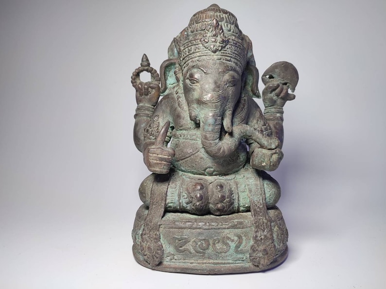 May include: A green bronze statue of Ganesha, the Hindu god of wisdom and prosperity, seated on a base with intricate carvings. The statue has a trunk, large ears, and four arms, holding various objects.