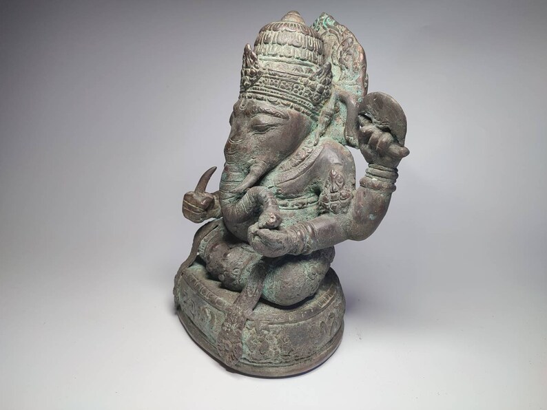 May include: A bronze statue of Ganesha, the Hindu god of wisdom and prosperity, seated on a base. The statue is intricately detailed and has a green patina.