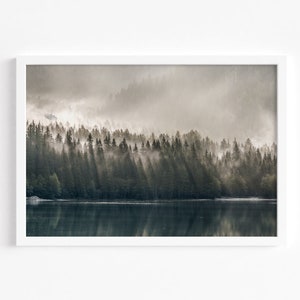 Może przedstawiać: Oprawiony wydruk krajobrazu leśnego, przedstawiający mglisty las, przez który przedziera się światło słoneczne, odbijające się w spokojnym jeziorze. Grafika jest prezentowana w białej ramie, podkreślającej naturalne piękno sceny.