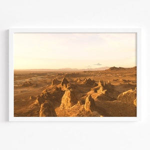 May include: A panoramic view of a desert landscape with tall, rocky formations in the foreground and a distant mountain range in the background. The sky is a soft, golden color, suggesting a sunset or sunrise.