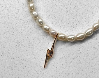 May include: A white pearl necklace with a gold lightning bolt charm.