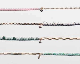 May include: Seven gold chain bracelets with different colored beads. The beads are pink, white with black speckles, light green, dark green, light blue, white, and purple.
