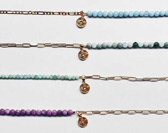 May include: Seven gold chain bracelets with different colored beads. The beads are pink, light blue, green, a darker green, purple, white with black speckles, and clear.