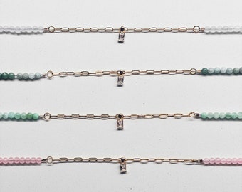 May include: Four gold chain bracelets with a small clear crystal pendant. Each bracelet features a different color of beads: white, light green, dark green, and pink.