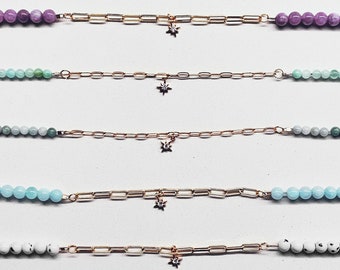 May include: A collection of delicate necklaces featuring a gold chain and a starburst pendant. Each necklace has a different color of gemstone beads, including purple, green, and white. The necklaces are displayed on a white background.