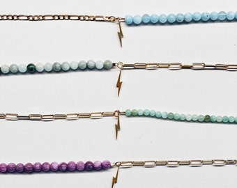 May include: Six gold chain bracelets with different colored beads and a lightning bolt charm. The beads are white, light blue, green, light green, purple, and white.