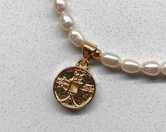 May include: A white pearl necklace with a gold coin pendant featuring Chinese characters. The coin is round and has a raised design.