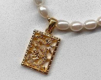 May include: A gold necklace with a pearl chain and a pendant featuring a detailed dragon design.