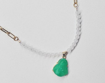 May include: A gold chain necklace with a green jade pendant. The pendant is carved with a detailed design. The necklace is strung with white beads.