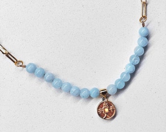 May include: A gold chain necklace with a light blue gemstone bead strand and a gold coin pendant with Chinese characters.
