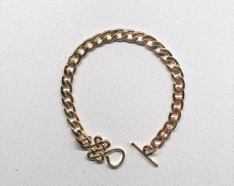 May include: A gold chain bracelet with a toggle clasp. The chain is thick and has a curb link design.