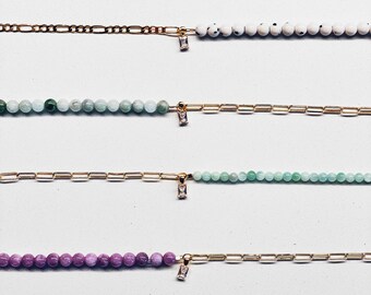 May include: Six gold chain bracelets with different colored beads and a small clear crystal charm on each. The beads are pink, white with black speckles, light green, dark green, purple, and light blue.