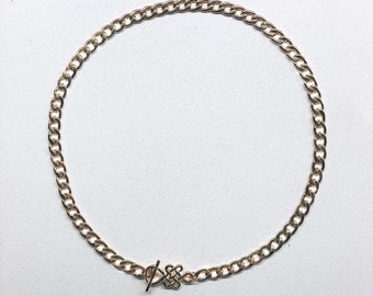 May include: A gold chain necklace with a toggle clasp. The chain is a curb style.